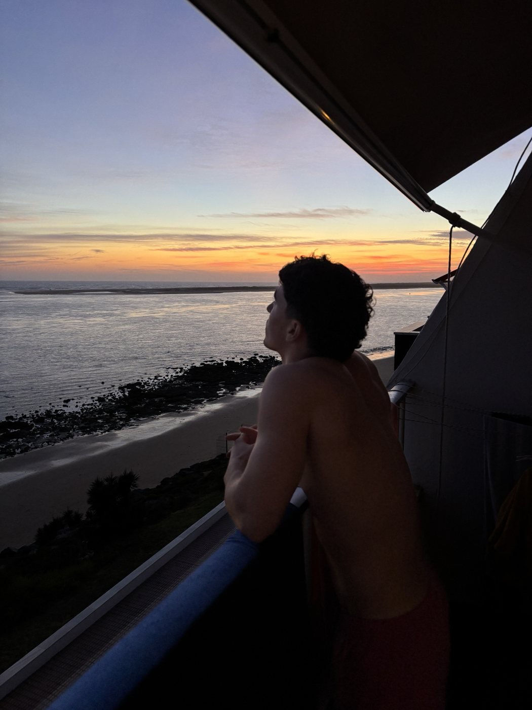 Juan mirando el atardecer sobre el mar desde un balcón